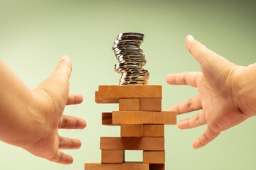Coin Stack on precariously Jenga blocks, hands protecting it, symbolizing fragile financial stability and economic uncertainty, need for caution