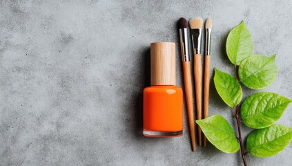 Orange nail polish, brushes, and leaves on a gray surface