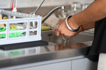 Close-up of a person washing hands under a faucet with running water in a clean kitchen sink with a dish rack and sponge nearby