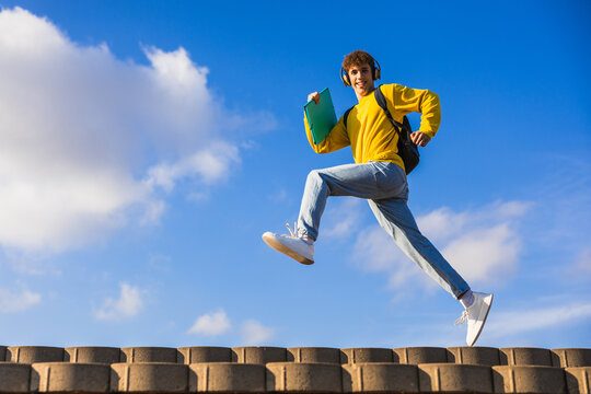 Happy college student running and listening music with headphones
