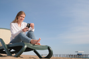 young woman sitting in the chaise lounge on the edge of the sea using smart phone