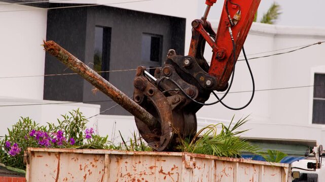 Excavator Claw Loads Palm Vegetation Into Skip Bin