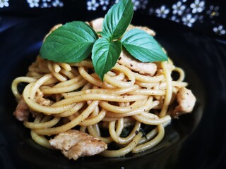 Stir-fried spaghetti with chicken and holy basil served on a black plate, garnished with fresh...