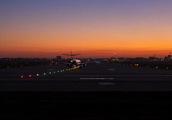 Fototapeta premium Airplane Landing at Sunset Aircraft Silhouette on Runway with Glowing Lights, Orange Sky, Aviation, Dusk, Travel, Flight