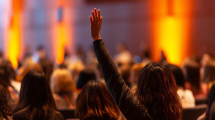 Rear view of diverse audience at a conference with focus on woman raising hand to ask a question or comment in business seminar