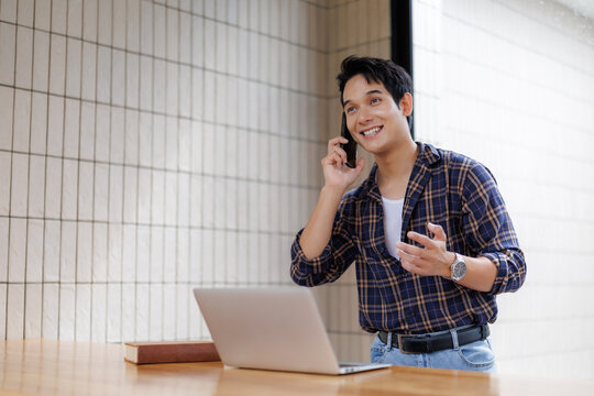 Young man talking on phone and working on laptop in cafe