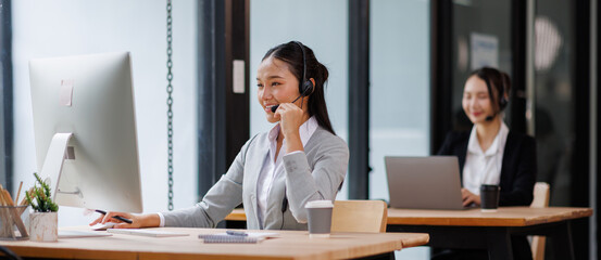 Asian Woman Wearing Headset Sitting At Desk Working In Office Call Centre Team
