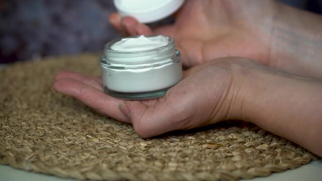 Woman&rsquo;s hand holding a glass jar with homemade natural face or body cream. Minimalist skincare concept with organic cosmetic on beige and dark background, eco-friendly and clean beauty style.