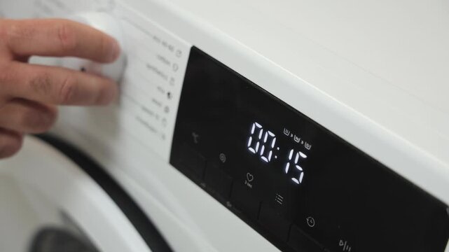 Hand adjusting washing machine settings for optimal clothes cleaning, showcasing modern technology and user-friendly interface with timer display