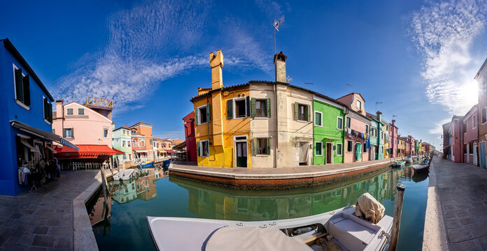 Brightly colored houses reflect in the serene canal of Burano, Venice during a clear sunny day