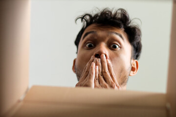 Surprised Young Man Peeking Into Open Box Reacting To Unexpected Delivery Or Discovery