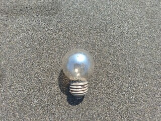 An old light bulb lying on the black sand beach in Jembrana, Bali, symbolizing ocean waste and environmental concerns.
