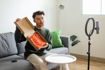 Young Asian Man Unboxing Orange Shirt For His Social Media Audience While Recording Product Review