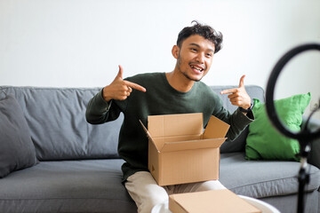 Excited Male Influencer Pointing At Product In Cardboard Box During Live Video Review