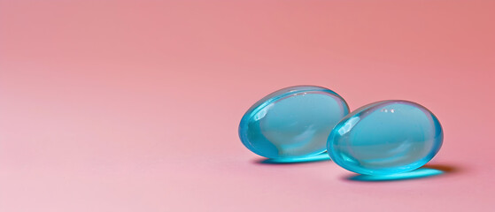 Two smooth blue soft gel capsules are positioned closely on a pastel pink background, showcasing their glossy texture and inviting appearance for pharmaceutical or wellness contexts