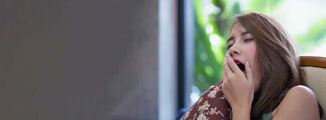 Sleepy Asian woman yawning in cozy home interior during the day, showing tiredness and need for rest in natural setting, Tired woman lifestyle.