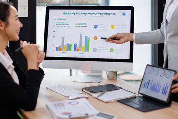 Asian business documents on office table with laptop computer and graph financial with social network diagram and three colleagues discussing data in the background
