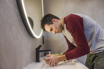 Young man carefully washes his hands in a modern bathroom, promoting hygiene, health, and responsible daily habits in a clean and organized environment.