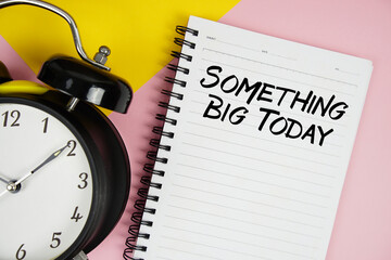 Something Big Today text written on notepad with alarm clock on pink background