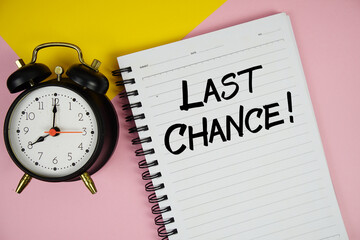 Last Chance! text written on notepad with alarm clock on pink background
