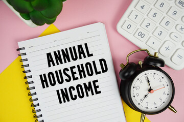 Annual Household Income text written on notepad with calculator and alarm clock on pink background