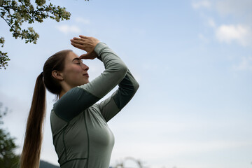 Meditation in nature. Silhouette of calm young woman with long hair meditating with a blue sky background, holding her hands in namaste at the forehead, wearing long sleeve, outdoor yoga activities