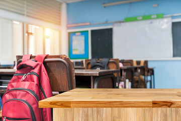 Red Backpack Hanging on Chair in Empty Classroom with Wooden Desk in Foreground and Whiteboard Behind
