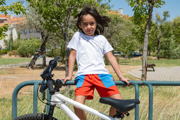 Obraz premium Young boy sitting on a fence with his bicycle in a park