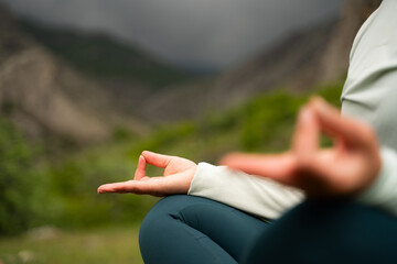 Calm in the storm. Woman meditating in nature against the backdrop of a stormy sky in the mountains, doing Padmasana exercise, sitting in lotus pose with mudra gesture outdoors close-up