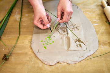 Removing flowers and leaves from clay to reveal detailed botanical imprints for plaster relief. Hands delicately lifting plants with tweezers during DIY floral art step-by-step tutorial