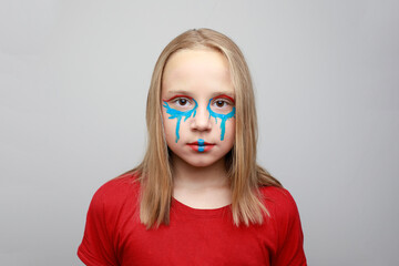 Creative girl child with vibrant blue and red face paint makeup on her cheeks and forehead....