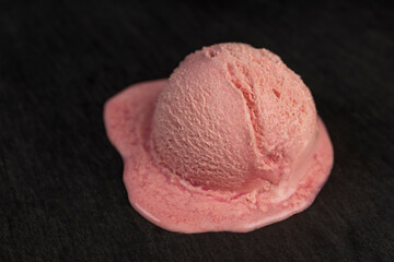 melting pink ice cream on a black board close up , sweet cold pink ice cream with strawberry flavor
