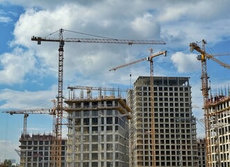 Multiple cranes work to construct high-rise buildings against a partly cloudy sky. Concept of: City development.
