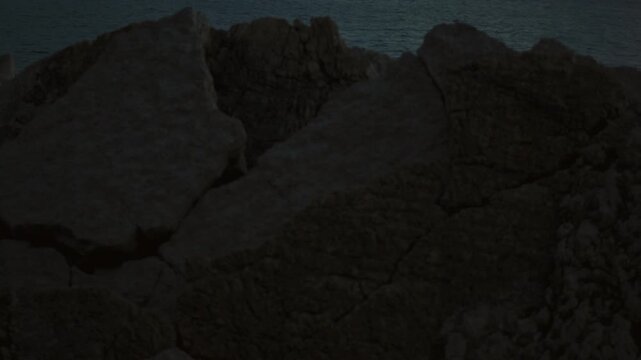 The camera slowly pans out from behind a coastal rock revealing a view of the evening Sveta Nedjelja Island in Petrovac, Montenegro.
