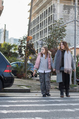 Cheerful mother and daughter hold each other's hand and cross the road at a crosswalk