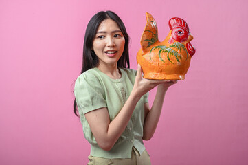Asian woman smiling while lifting a large orange ceramic rooster to shoulder level with both hands...