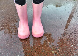 Pink rubber boots stand in a puddle reflecting the surroundings. Concept of Childhood adventure.