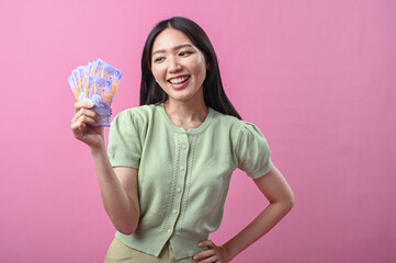 Asian woman in green top smiling confidently while holding a fan of purple Indonesian banknotes in...