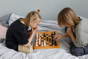 Little brother and sister playing indoor. Two cute children playing chess at home