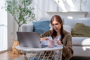 woman working on her laptop at home, focused on her tasks while sitting on floor. cozy atmosphere...