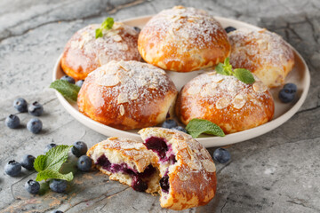 Homemade French brioche buns with blueberries and almond petals close-up in a plate on the table. Horizontal