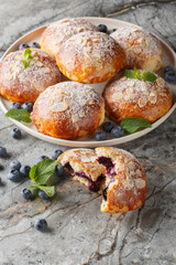Fresh baked almonds buns filled with blueberry closeup on the plate on the table. Vertical