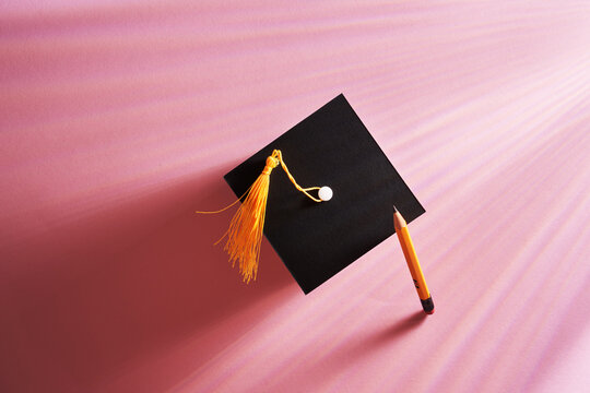 small mortarboard and pencil against pink background
