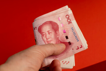 holding a large stack of Chinese yuan in his hand on a red background, holding a large amount of...