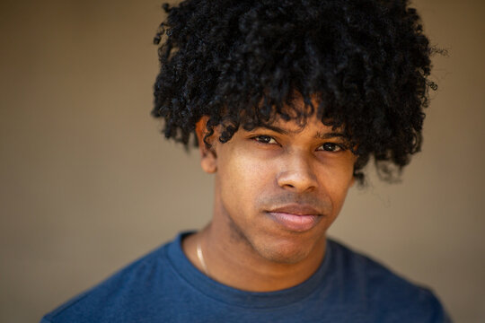 Serious young man with curly hair in studio-style portrait with neutral background