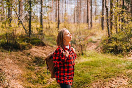 A girl in a red shirt and with a backpack is walking in the forest. Hiking in sunny autumn forest.