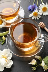 Aromatic herbal tea in glass cups and different flowers on black table, above view