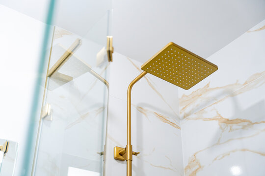 Zoom sur les diff&eacute;rents &eacute;l&eacute;ments d&rsquo;une salle de bain moderne avec marbre blanc &agrave; rainures dor&eacute;es, colonne de douche, robinetterie et accessoires en finition bronze dor&eacute;.