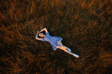 Woman relaxing in a grassy field during sunset in a light blue dress