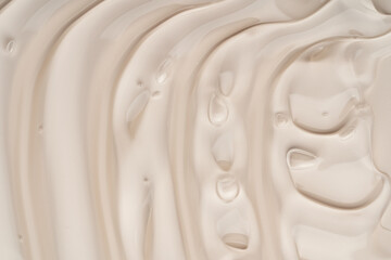 Close-up shot of beige liquid cosmetic gel or serum makeup swatches with a glossy, shiny texture on a smooth beige background.